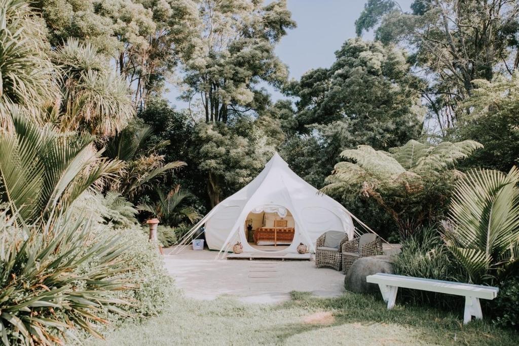 a white tent with a bench and trees at Belle Glamping by the Sea in Katikati