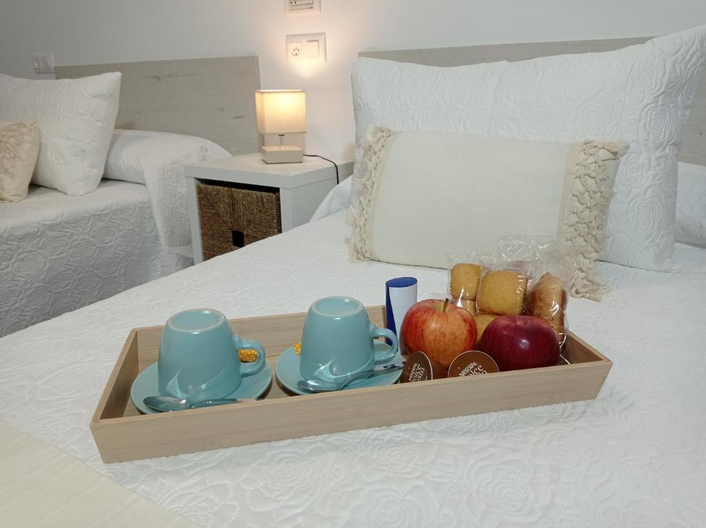 un vassoio di cibo con mele e tazze su un letto di Martínez Rooms Pilgrims a Caldas de Reis