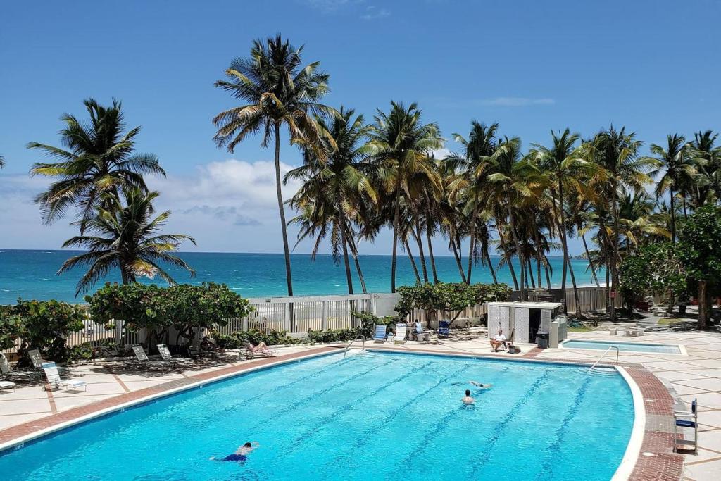 a swimming pool with palm trees and the ocean at KASA Las Palmas studio apt for 2 OCEAN VIEW BEACHFRONT CONDO POOL in San Juan