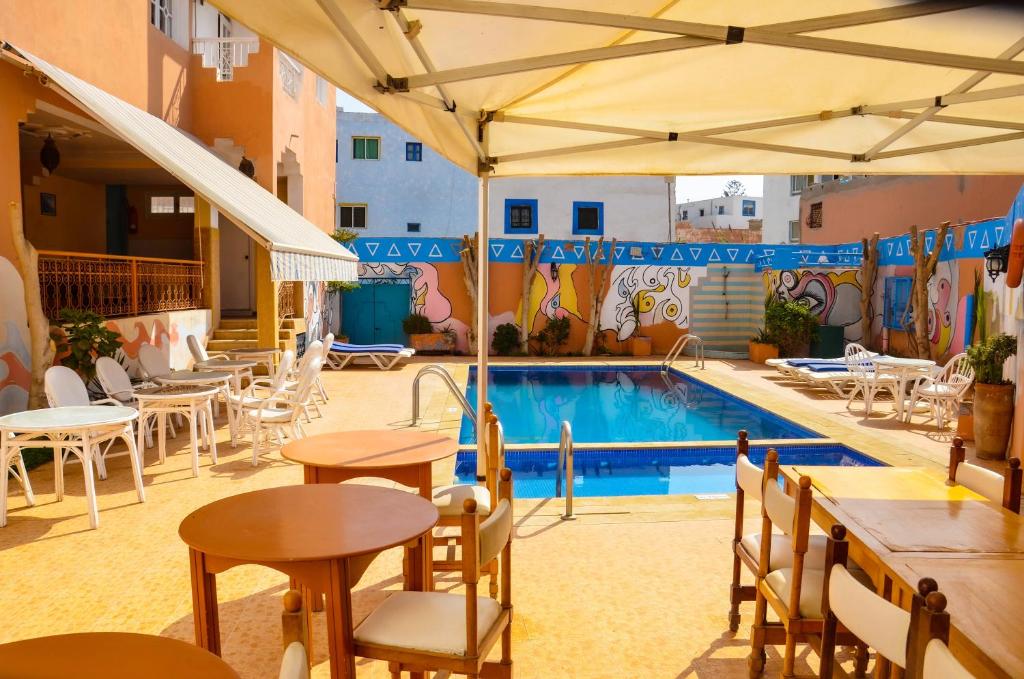 una piscina con mesas y sillas junto a un edificio en Hôtel Auberge du Littoral, en Aourir