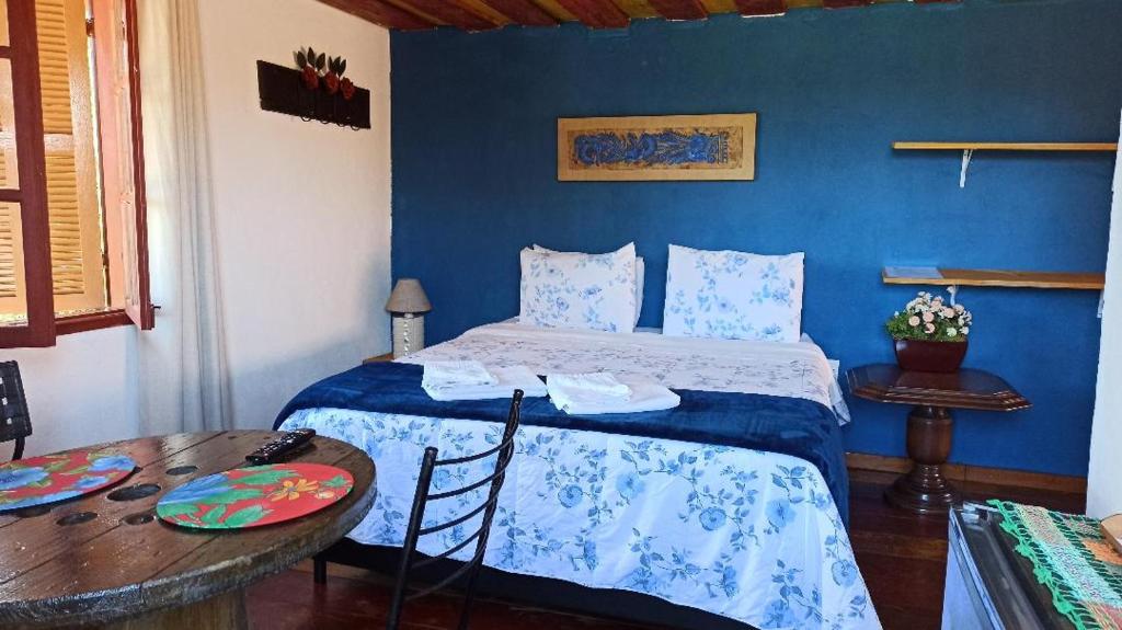 a blue bedroom with a bed and a table at Pousada Esquina de Lavras in Lavras Novas