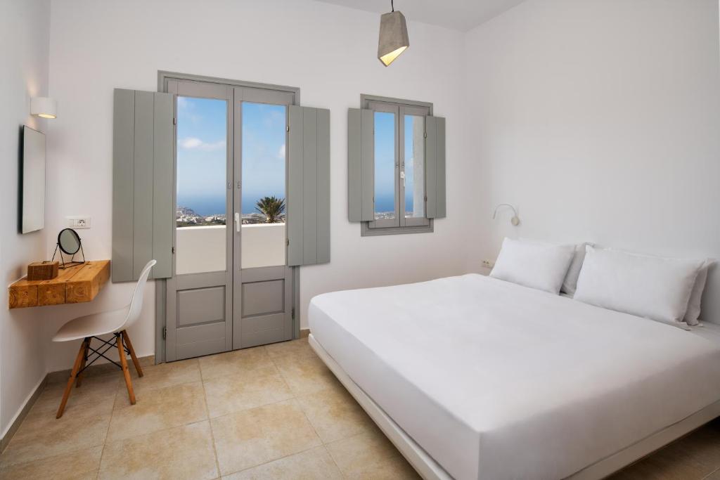 a white bedroom with a bed and a desk at Astivi Santorini Apartments in Pyrgos