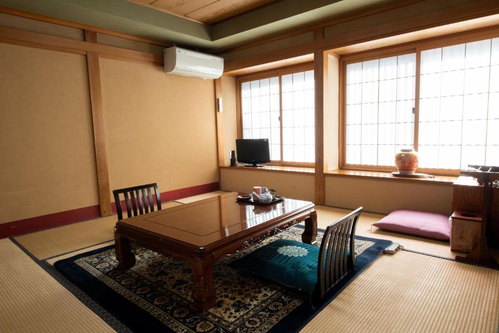 a living room with a table and chairs and windows at Jizokan Matsuya Ryokan in Nagano