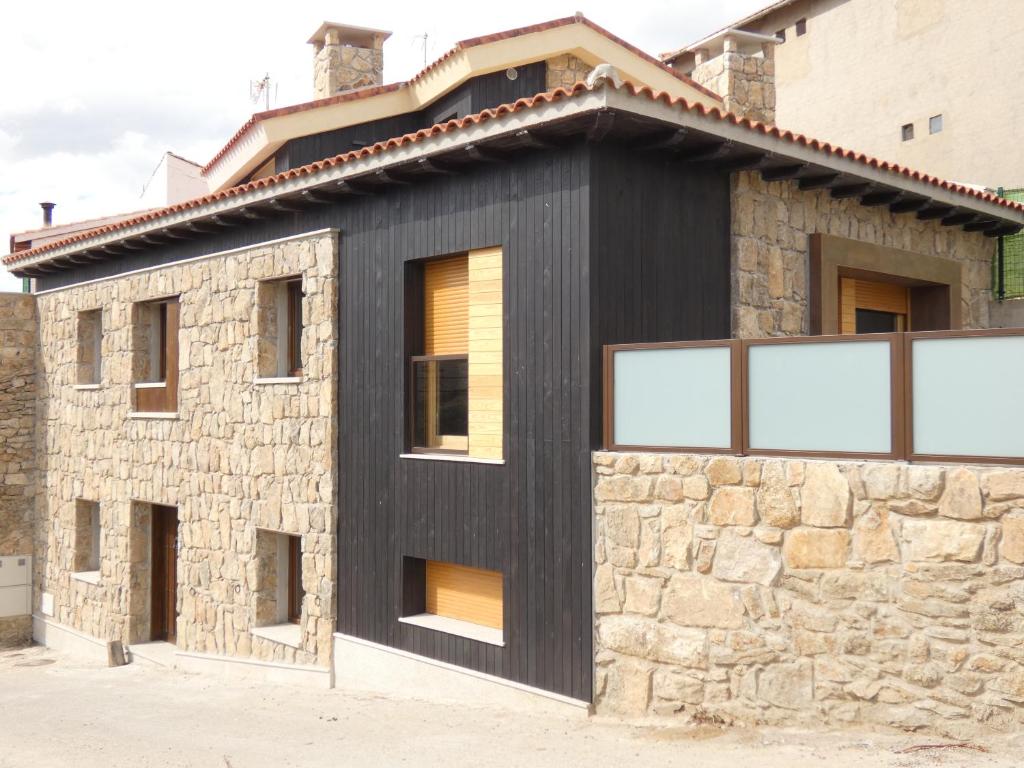 Casa negra con ventanas y pared de piedra en Casa Rural A Ritmo De Burro, en Robledondo