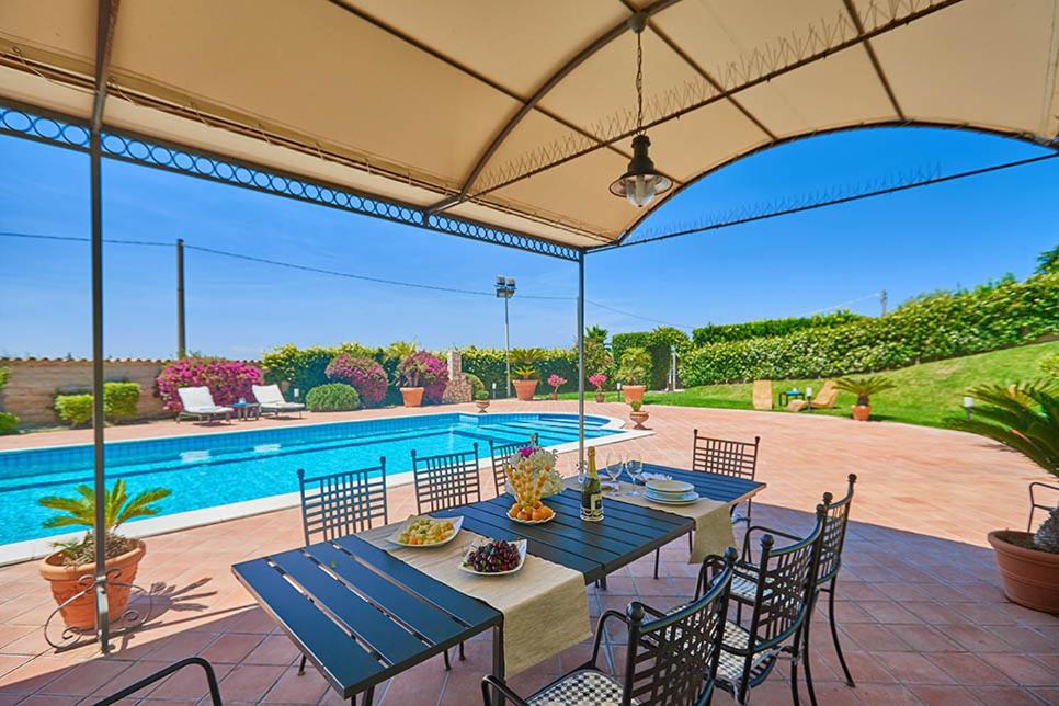 um pátio com uma mesa e cadeiras e uma piscina em Villa Dinira em Catânia