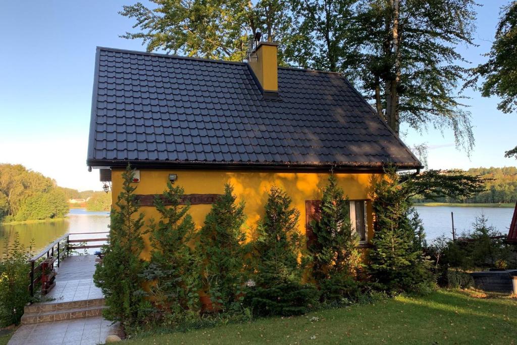 a yellow house with a black roof next to a lake at Holiday Home on Lake Marchowo with Terrace in Koleczkowo