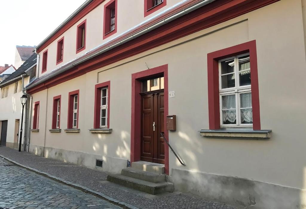 a white building with a red door on a street at Pension Torgau in Torgau