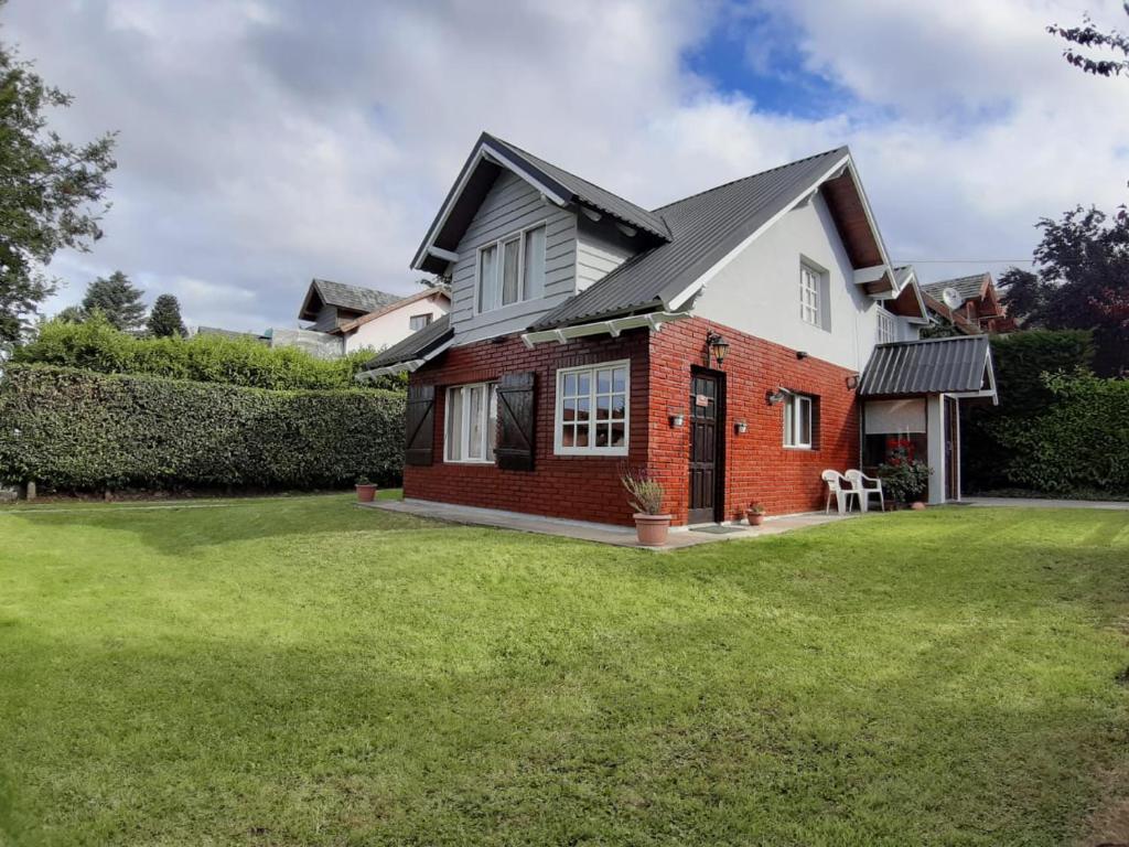 une maison en brique rouge avec une cour d'herbe dans l'établissement Melipal Flats, à San Carlos de Bariloche