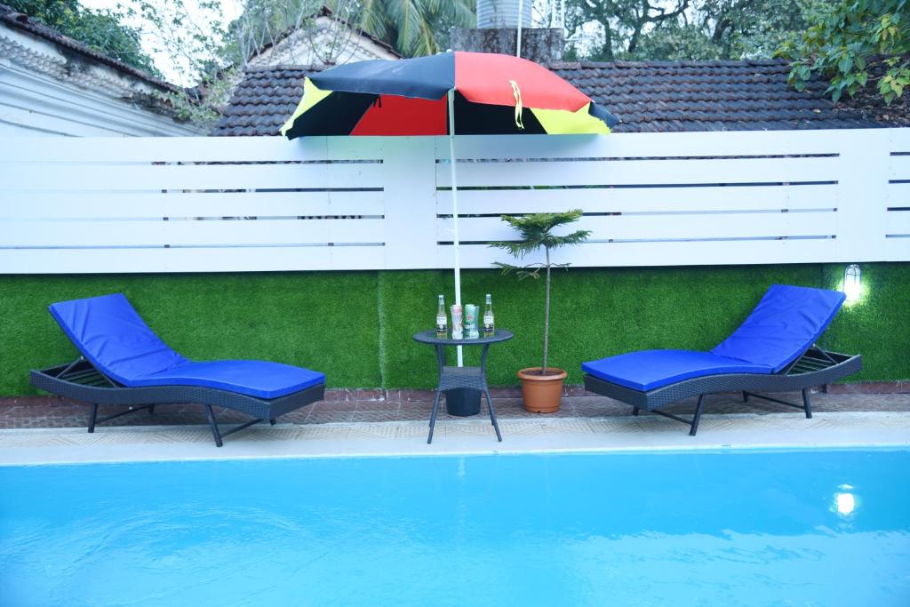 due sedie e un tavolo con ombrellone accanto a una piscina di Clarissa Resort Goa a Saligao