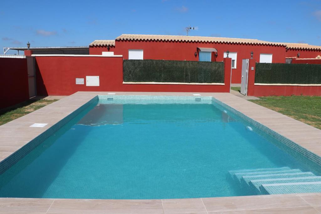 een zwembad voor een rood huis bij Chalet Brisa Veraniega in Conil de la Frontera