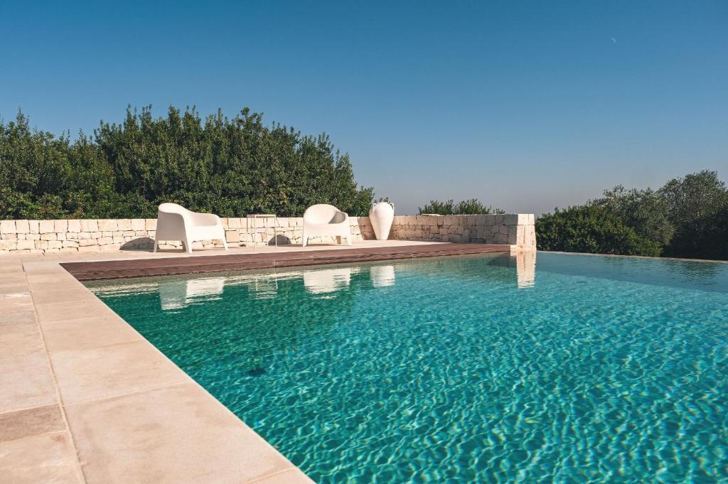 una piscina con 2 sillas blancas y una piscina en HelloAPULIA - Panoramic Masseria Minetta with private pool, en Cisternino