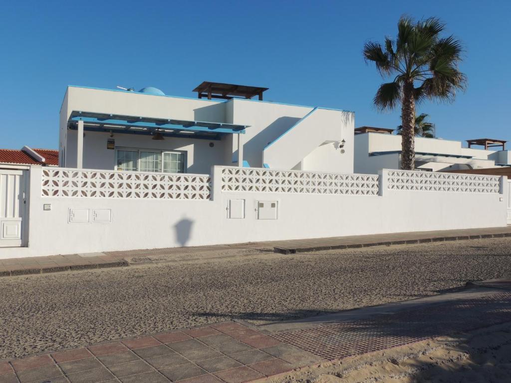 une maison blanche avec une clôture et un palmier dans l'établissement View , Beach House , by MAHBOVILLAS, à Corralejo