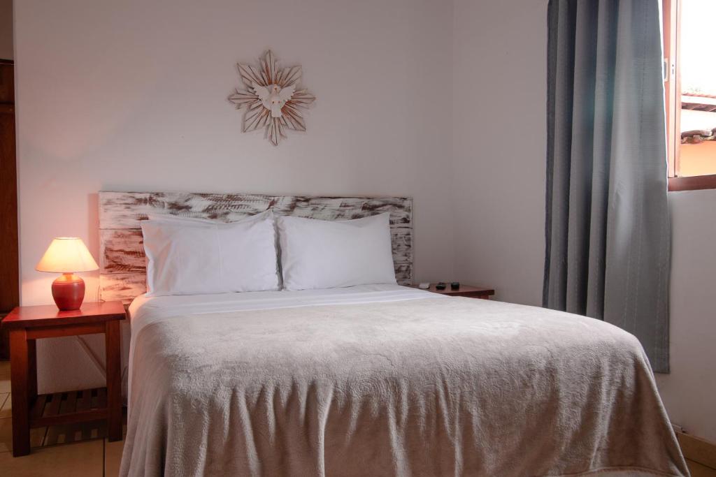 1 cama con sábanas blancas y reloj en la pared en Pouse no Jardim, en Pirenópolis