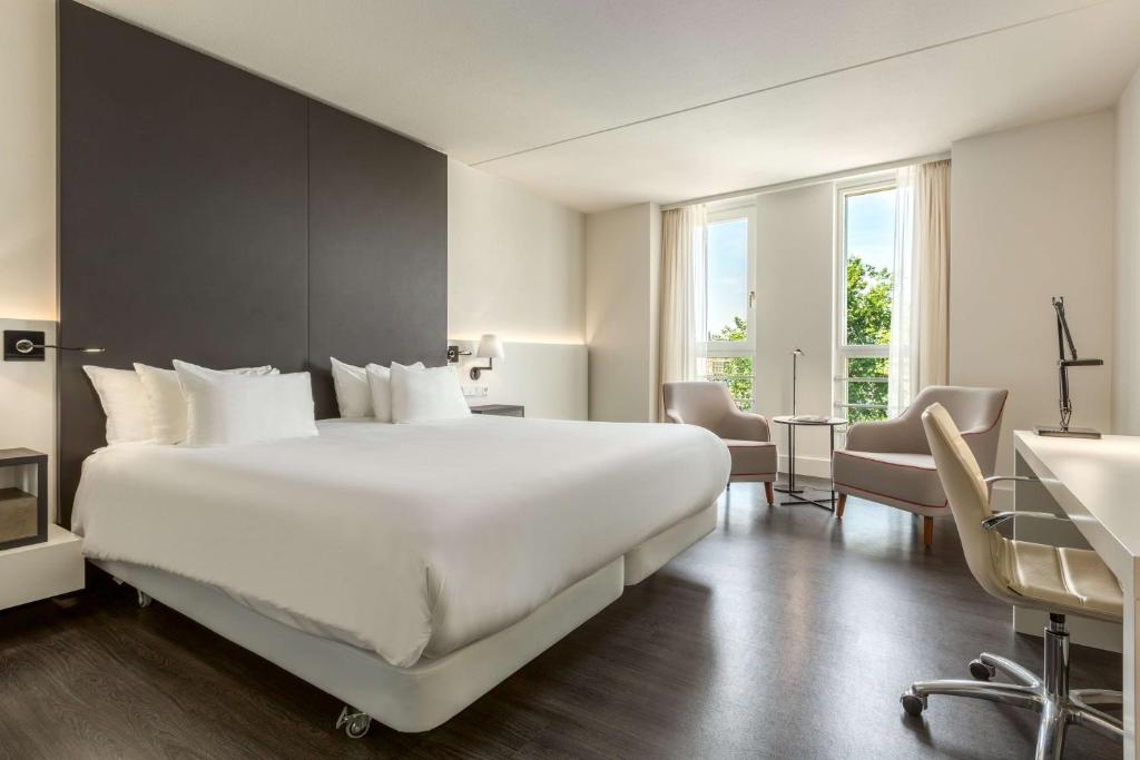 ein Hotelzimmer mit einem großen weißen Bett und einem Schreibtisch in der Unterkunft NH Collection Amsterdam Barbizon Palace in Amsterdam