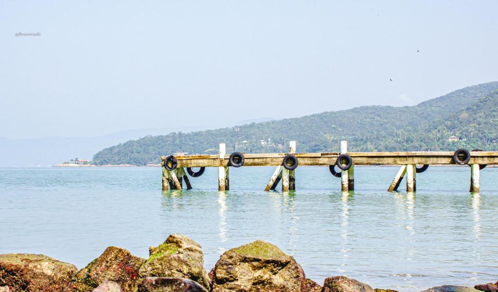 a dock in the water with rocks in the foreground at Pousada Casa do Oscar in Governador Celso Ramos
