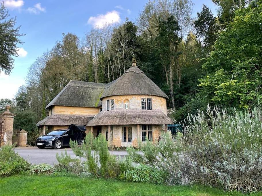 ein altes Haus mit einem Strohdach und einem Auto in der Unterkunft Round Lodge Dorset in Sherborne