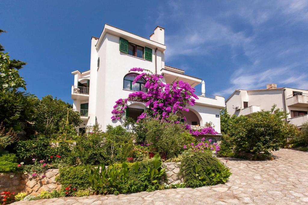 a white house with purple flowers in front of it at Apartments Delfin in Krk