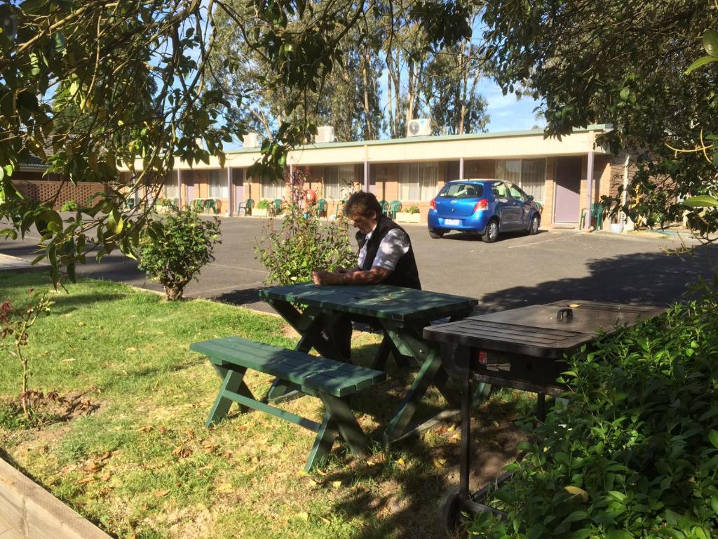 mężczyzna siedzący przy stole piknikowym przed budynkiem w obiekcie Woodmans Hill Motel w mieście Ballarat