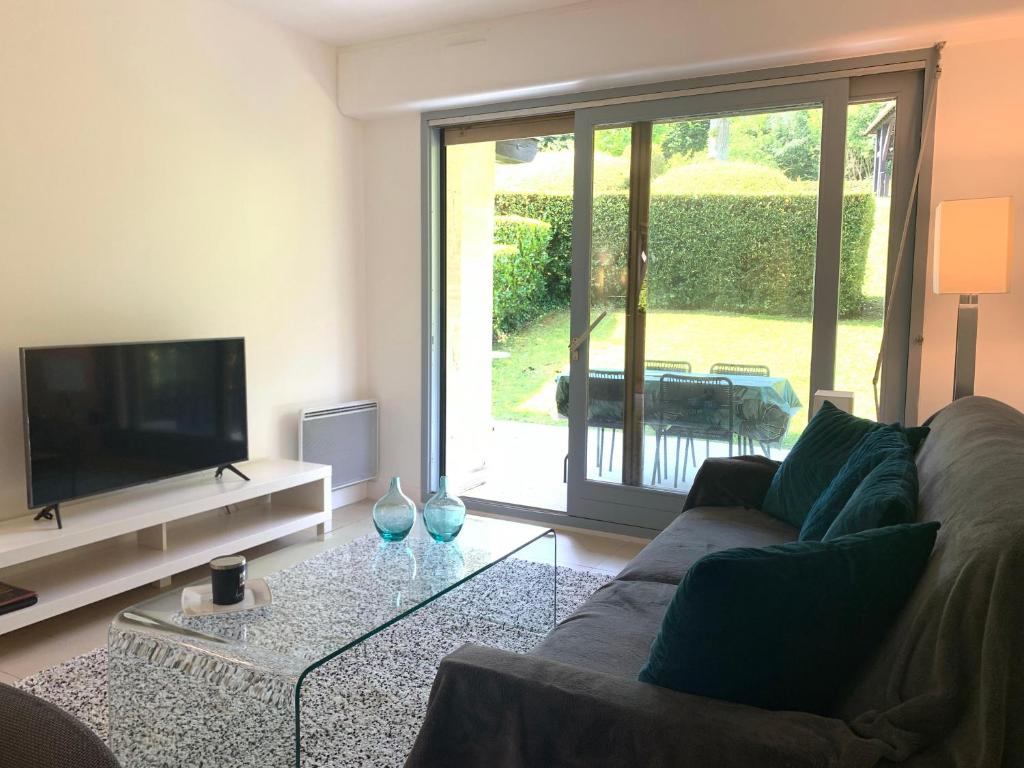 ein Wohnzimmer mit einem Sofa und einem TV in der Unterkunft Rez-de-jardin - Résidence avec Piscine - Deauville in Deauville