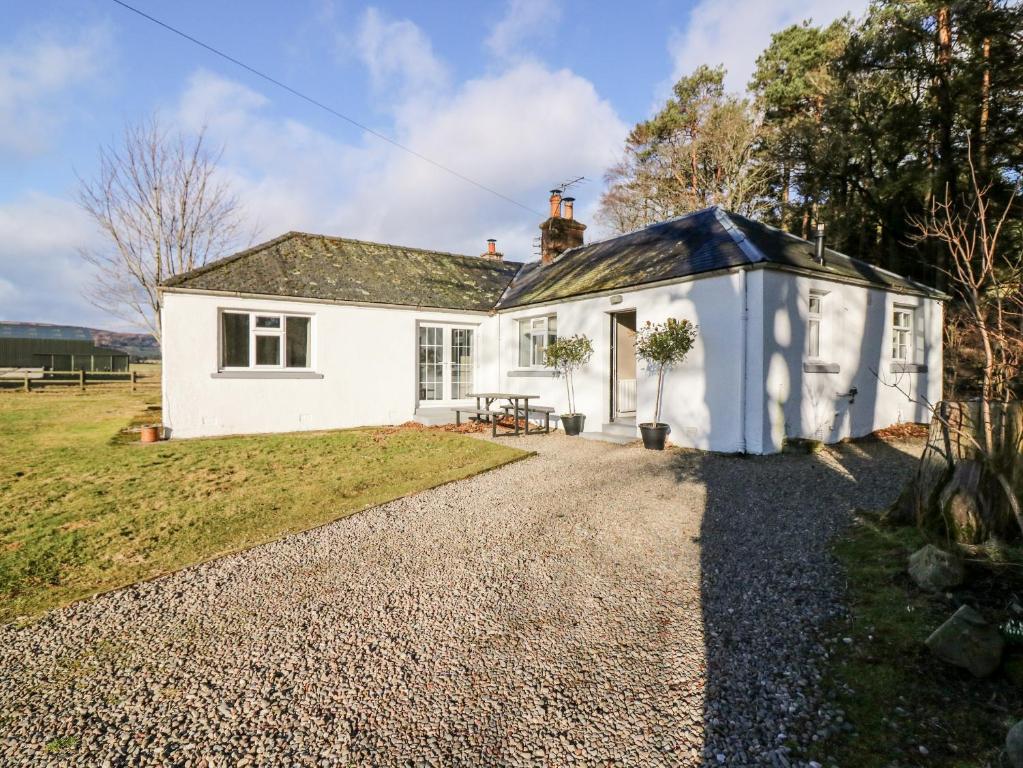 a white cottage with a gravel driveway at White Hillocks Cottage in Inchmill