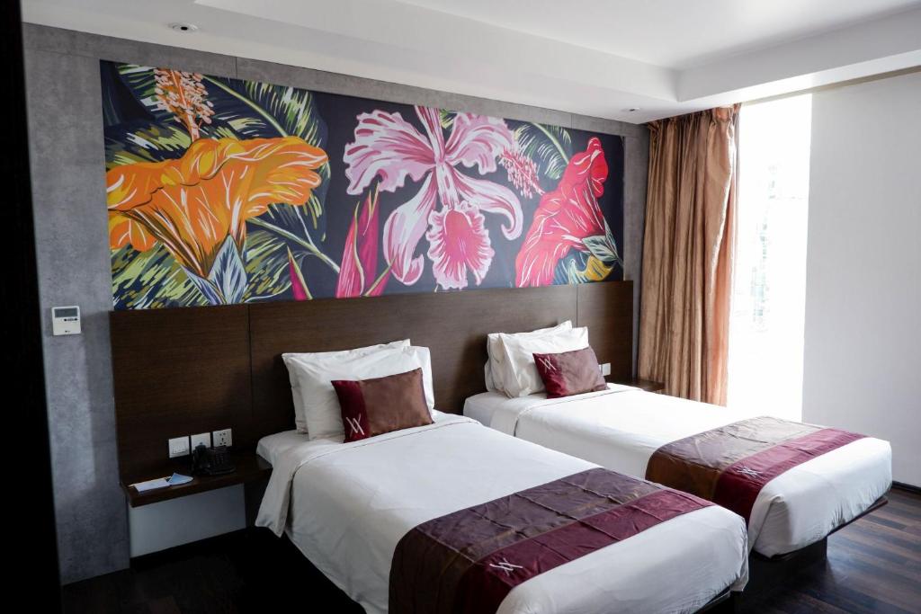 two beds in a hotel room with a painting on the wall at Akmani Hotel Jakarta in Jakarta