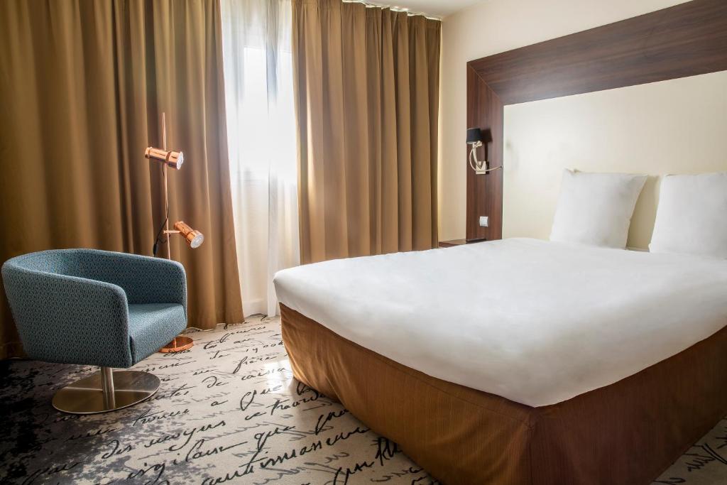 Cette chambre comprend un grand lit et une chaise bleue. dans l'établissement Mercure Paris Porte d'Orleans, à Montrouge