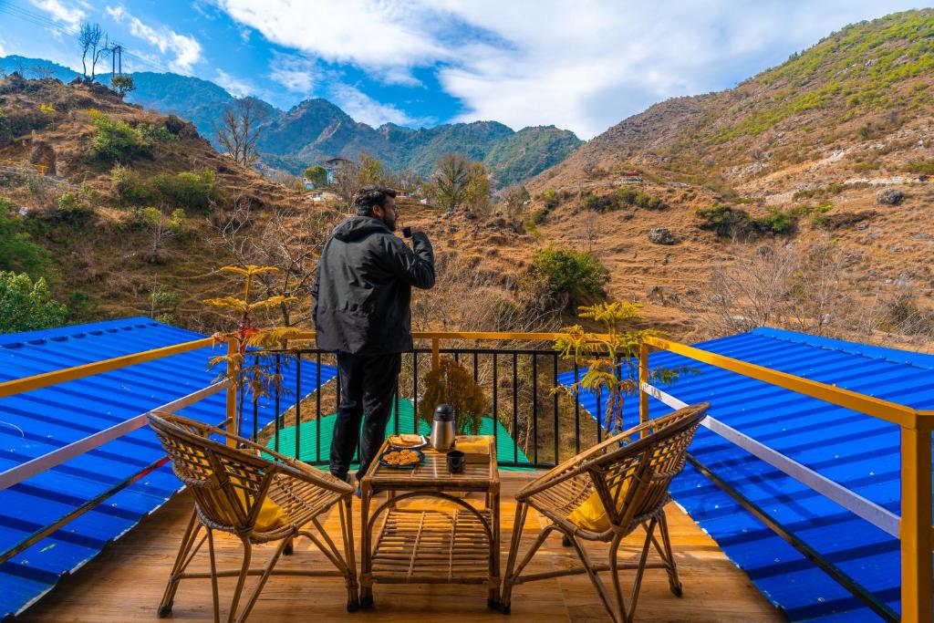 a man standing on a deck with a table and chairs at The Hosteller Mussoorie By the Streamside, Kempty in Mussoorie