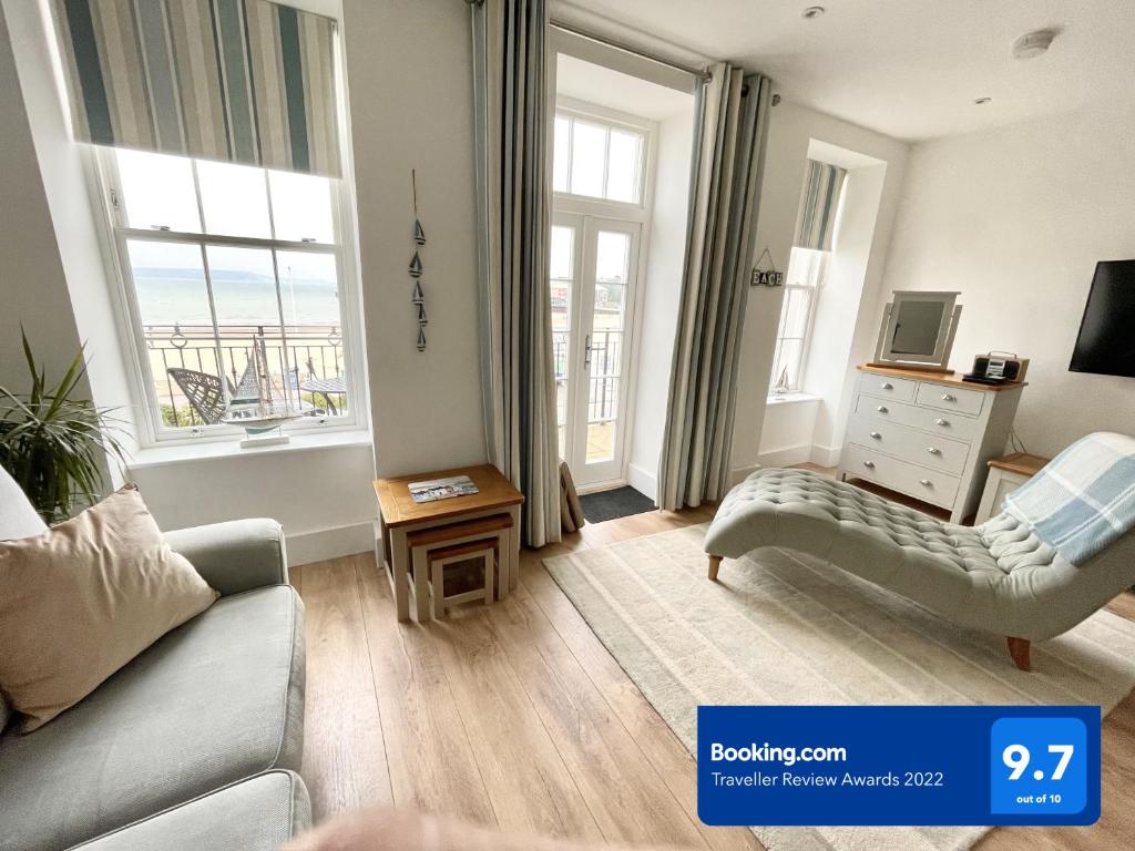 a living room with a couch and a chair and windows at Beachfront with balcony 1st Floor apartment "The Beaches" in Weymouth