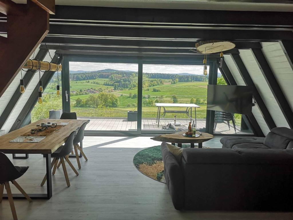 ein Wohnzimmer mit einem Tisch und einem großen Fenster in der Unterkunft Ferienhaus Fynnhütte in Schwarzenborn