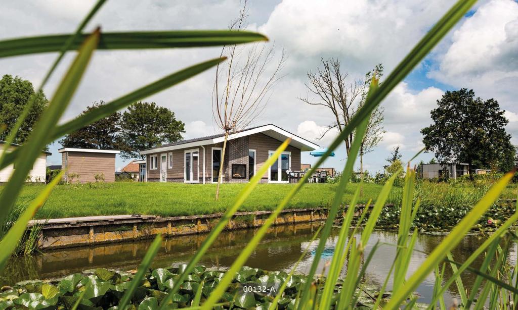 a house on the side of a river with tall grass at TopParken – Park Westerkogge in Berkhout