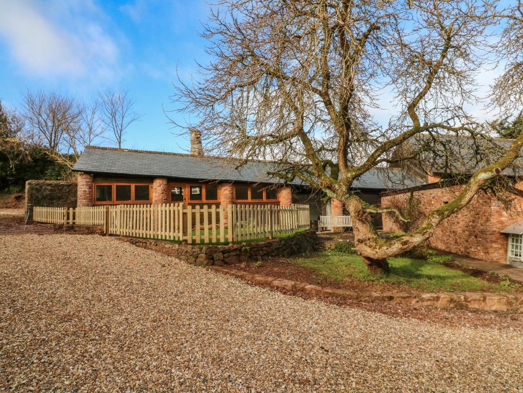 una casa in mattoni con una recinzione e un albero di Middle Burrow Cottage a Minehead