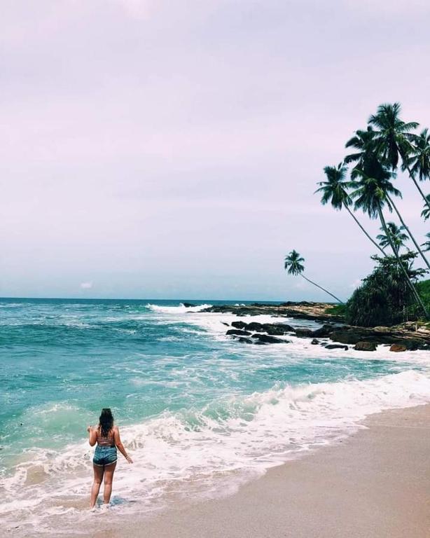 a woman standing in the water on a beach at Goyambokka Guesthouse in Tangalle