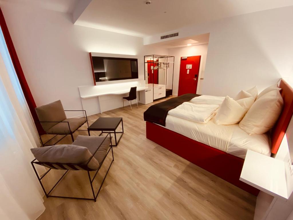 um quarto de hotel com uma cama e uma televisão e cadeiras em DORMERO Hotel Hof em Hof