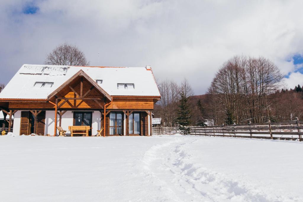 a house with a snow covered roof in a field at Cinege Vendeghaz/Casa de oaspeți Pițigoi in Izvoare