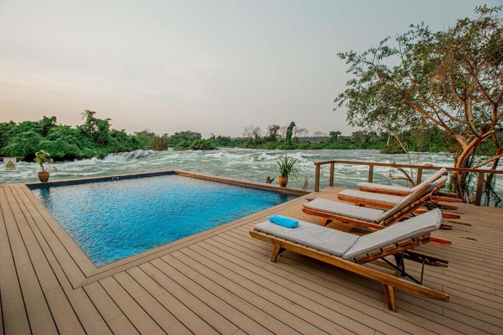 a deck with a pool and lounge chairs next to a river at Lemala Wildwaters Lodge in Kangulumira