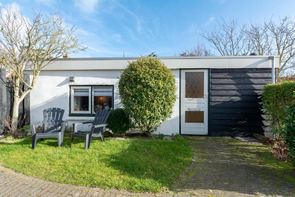 una pequeña casa blanca con 2 sillas en el patio en De Bunker - Callantsoog, en Callantsoog
