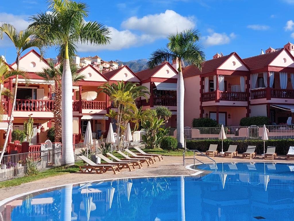 a resort with a swimming pool with chairs and palm trees at Residencia El Duque - 1, VILLA MARIUS in Adeje