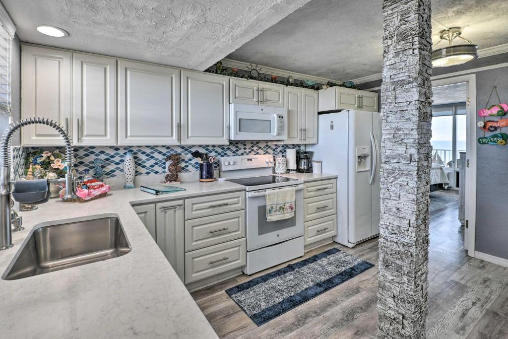 a kitchen with white cabinets and white appliances at Bright Daytona Beach Condo with Community Pool! in Daytona Beach