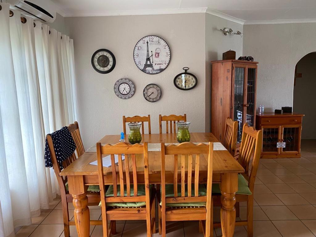 einen Esstisch mit Stühlen und eine Uhr an der Wand in der Unterkunft La Prima Casa in Graskop