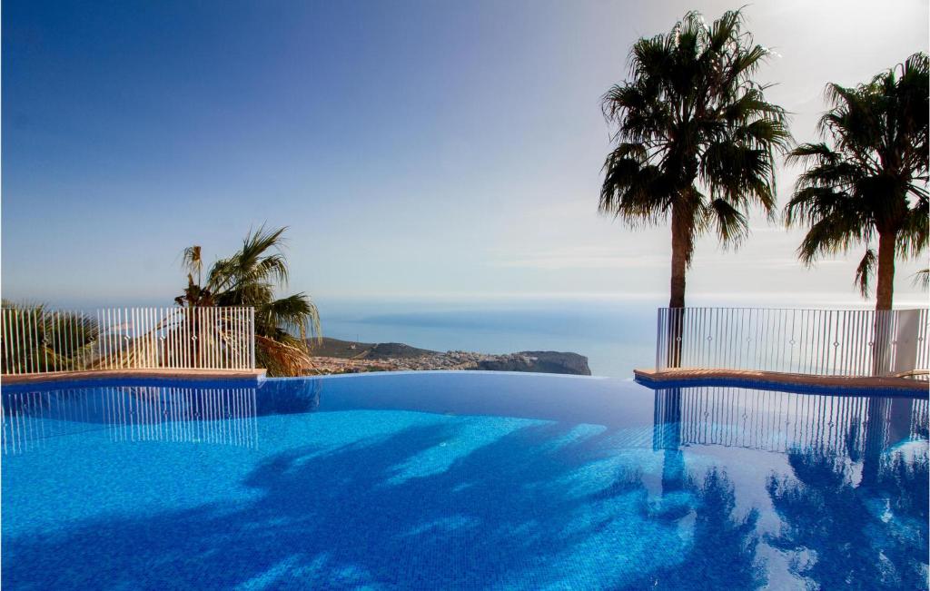 einen Pool mit einer Palme und dem Meer in der Unterkunft Nice Apartment In Cumbre Del Sol With Wifi in Cumbre del Sol