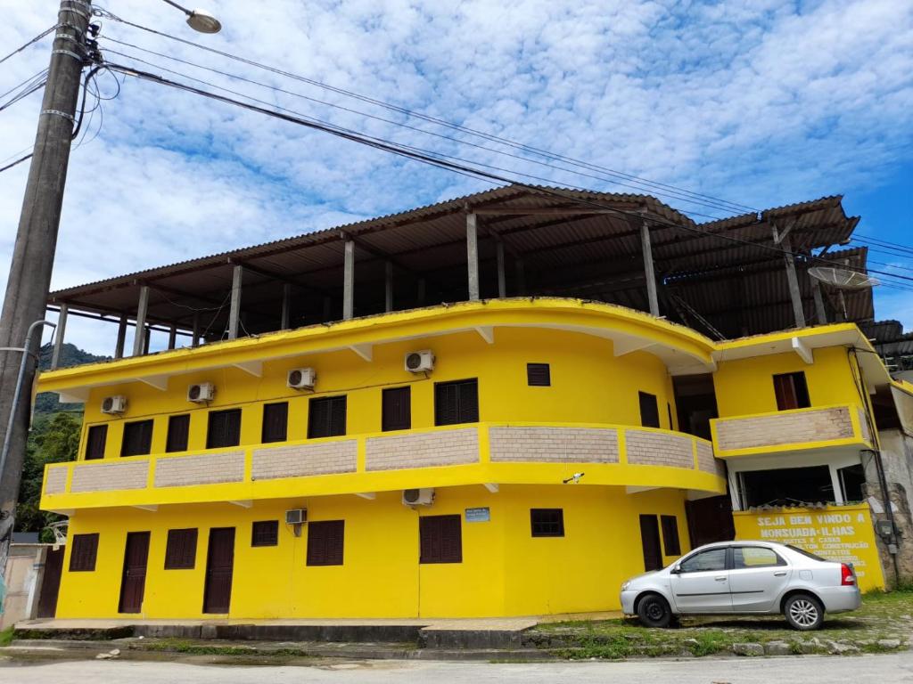 a yellow building with a car parked in front of it at Pousada Milton in Angra dos Reis