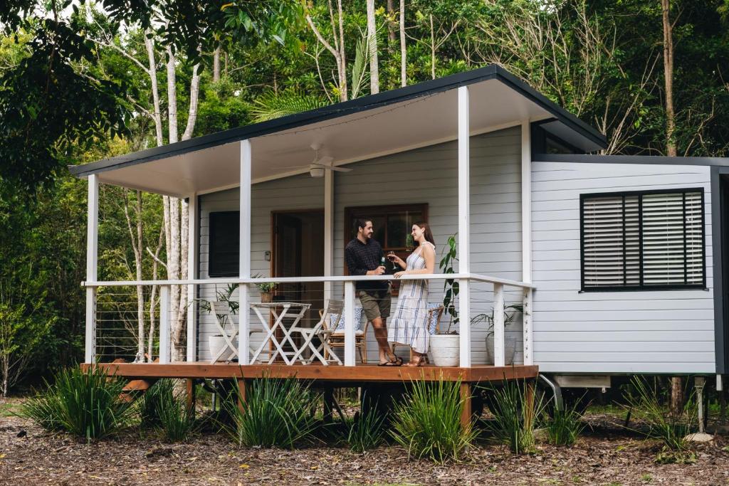 - un couple debout sur la terrasse couverte avant d'une petite maison dans l'établissement Maclean River Front Tiny House - Clarence Valley Tiny Homes, à Maclean