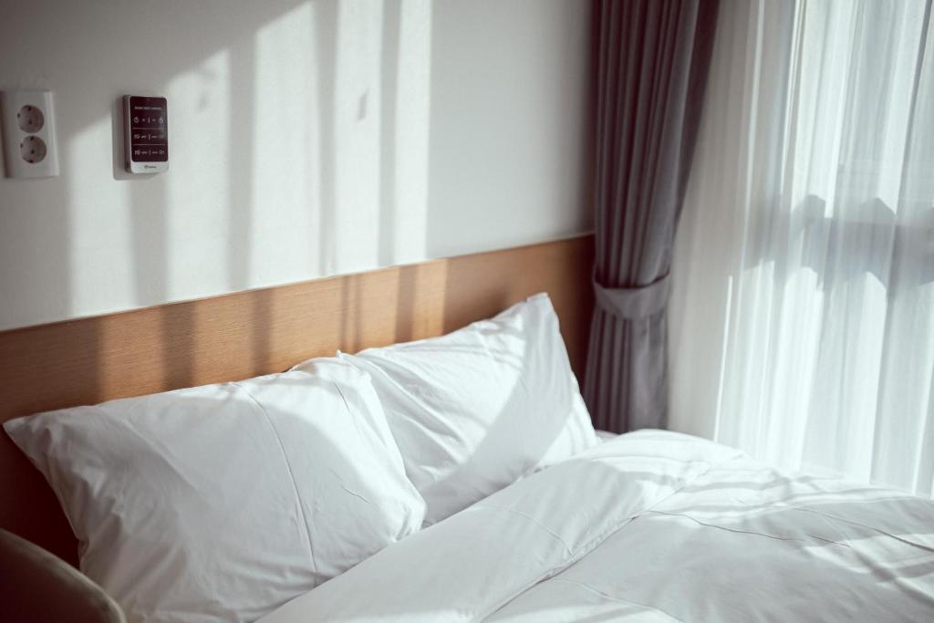 an unmade bed with white pillows next to a window at Kenny Stay Busan Gijang in Busan