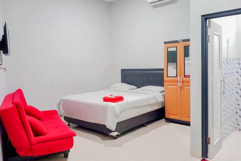 a bedroom with a bed and a red chair at Mahkota Residence Mitra RedDoorz in Karawang