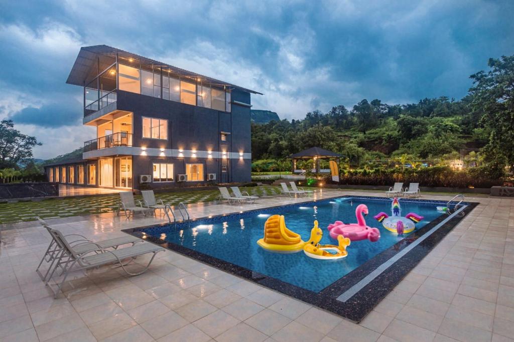 a house with a swimming pool with inflatable toys in it at SaffronStays Sundowner by the Lake, Karjat - party-perfect pool villa with rain dance and cricket turf in Karjat