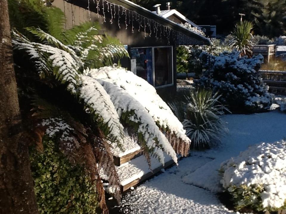 une brousse recouverte de neige à côté d'une maison dans l'établissement Tongariro Holiday Park, à Parc national