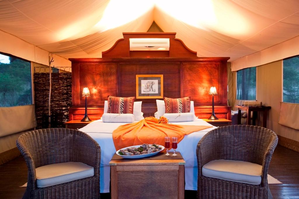 een slaapkamer met een groot bed en 2 stoelen bij The Springbok Lodge in wildreservaat Nambiti