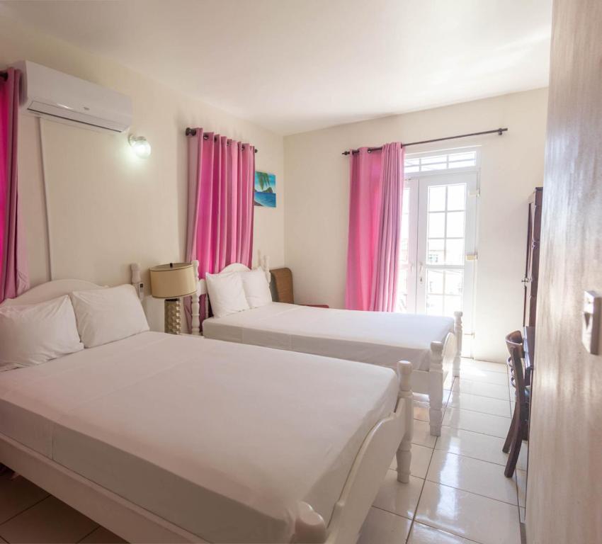 two beds in a room with pink curtains at St. James Guesthouse in Roseau