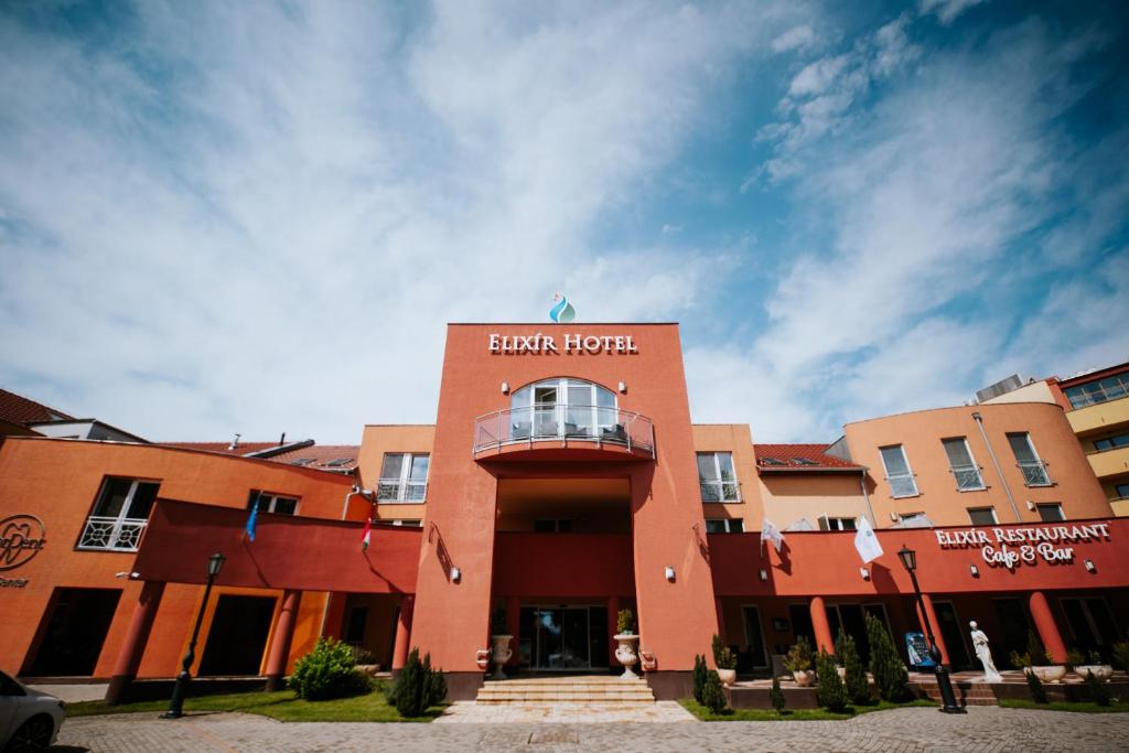 a red building with a clock on top of it at Elixír Medical Wellness Hotel in Mórahalom