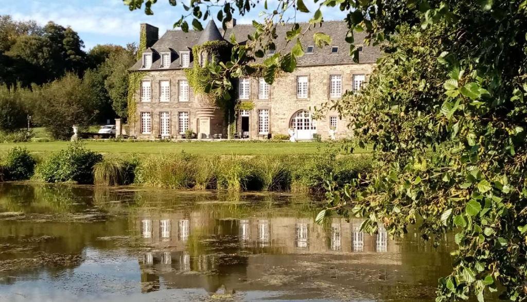 une vieille maison avec un étang en face de celle-ci dans l'établissement Château de la Motte Beaumanoir, à Pleugueneuc